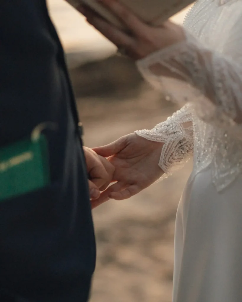 Close-up of the couple's hands and rings as they exchange private vows on the beach at Tupper Manor