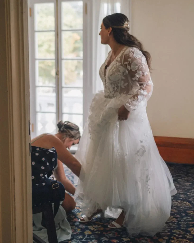 Bride steps into her gown beside a tall window in the bridal suite at Tupper Manor