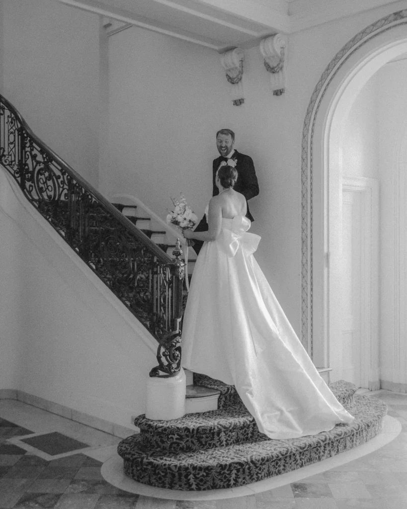 Bride descends the grand spiral staircase in the marble foyer at Tupper Manor