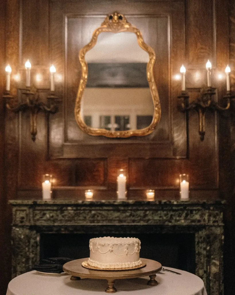 Wedding cake displayed in front of the candlelit fireplace in the Tupper Manor library