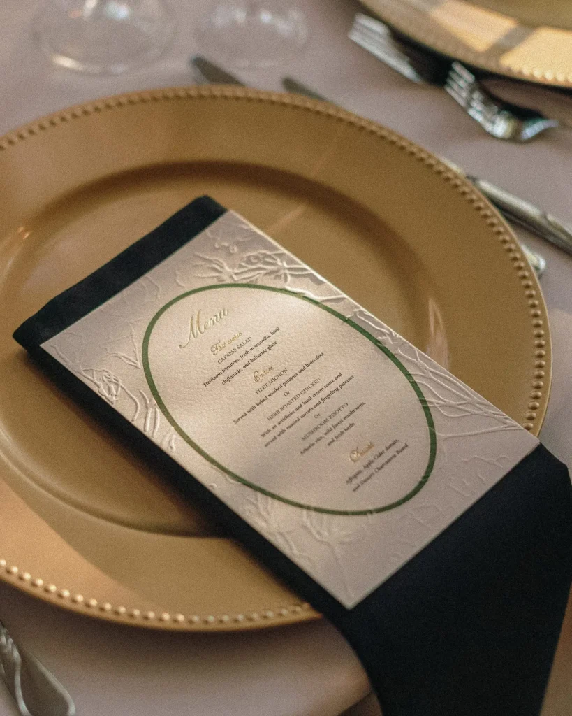 Place setting with a gold charger, black napkin and printed menu at a Tupper Manor wedding reception