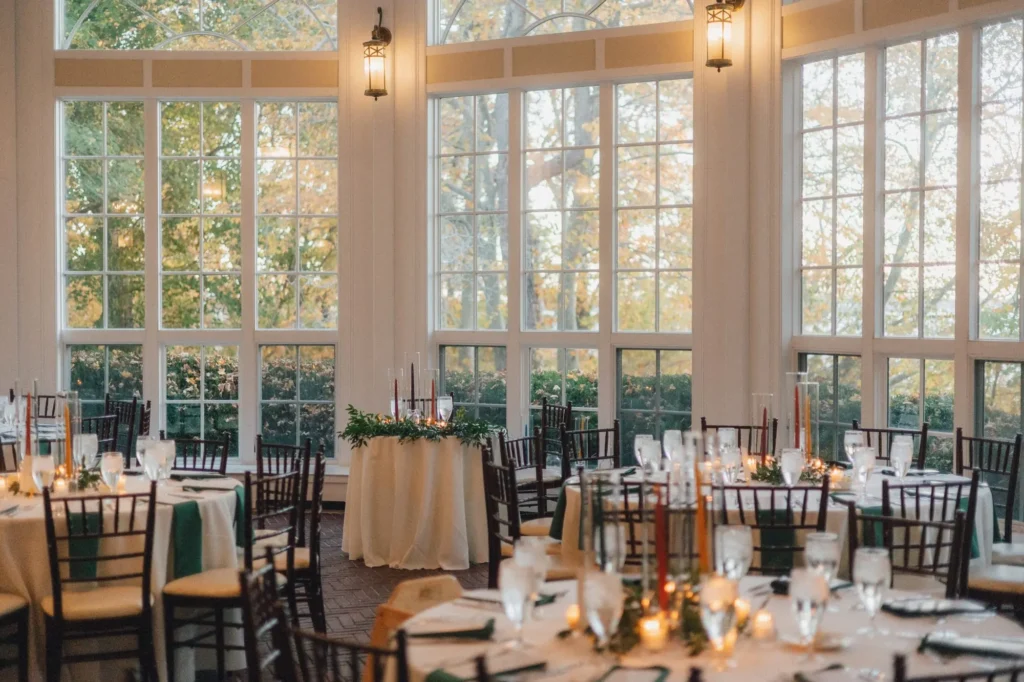 Tupper Manor conservatory set for a candlelit wedding reception with round tables and floor-to-ceiling windows