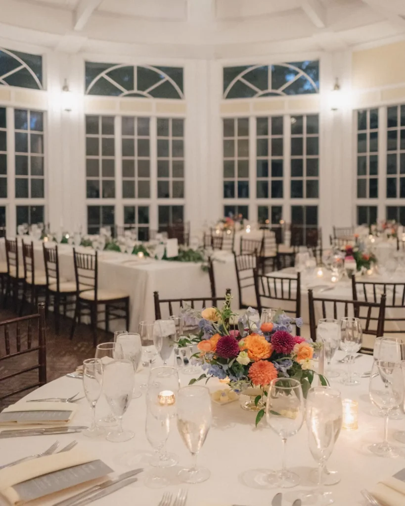 Colorful floral centerpiece on a candlelit table in the Tupper Manor conservatory with tall windows behind