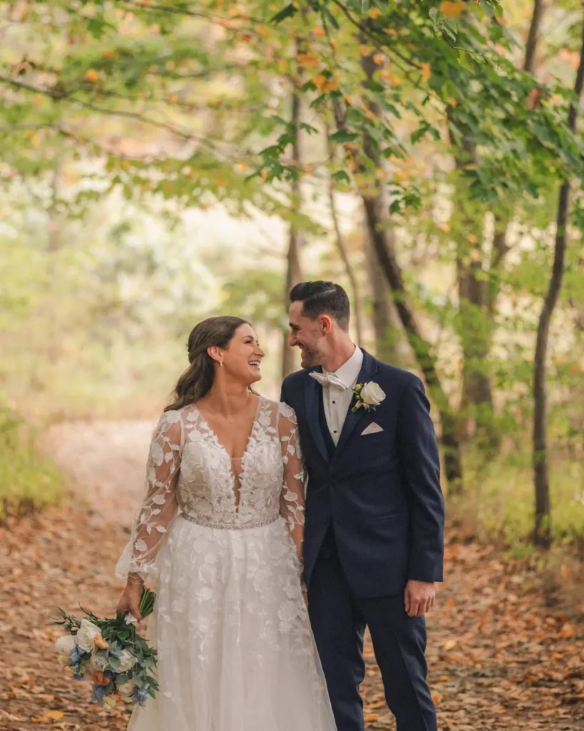 Bride and groom smile together on the wooded path behind Tupper Manor in fall