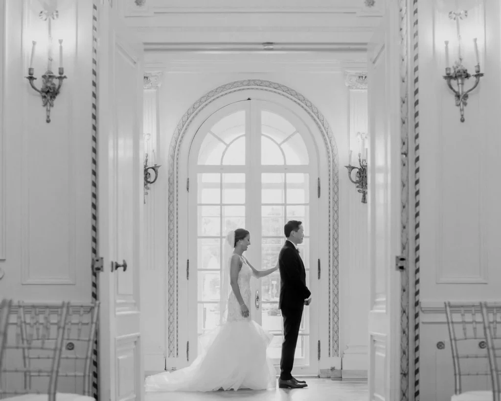 Bride taps the groom on the shoulder for a first look in front of the arched ballroom doors at Tupper Manor, black and white