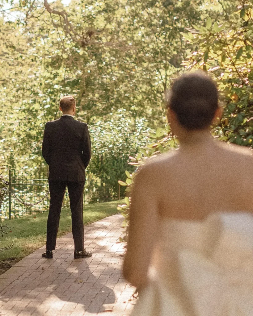 Bride approaches the groom from behind for a first look on the brick path behind Tupper Manor