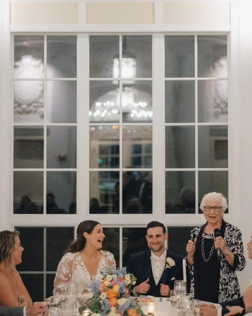 Grandmother raises a glass during a toast at a Tupper Manor wedding reception while the couple laughs