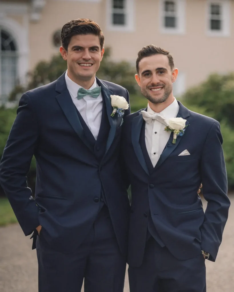 Groom and groomsman in navy suits with white boutonnieres on the grounds at Tupper Manor