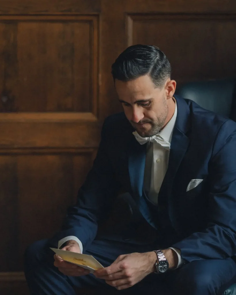 Groom reads a letter in a leather chair in the wood-paneled library at Tupper Manor