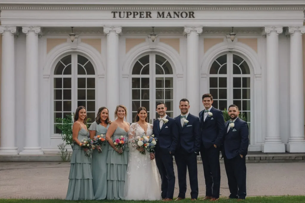 Wedding party in navy suits and sage dresses in front of the Tupper Manor columns