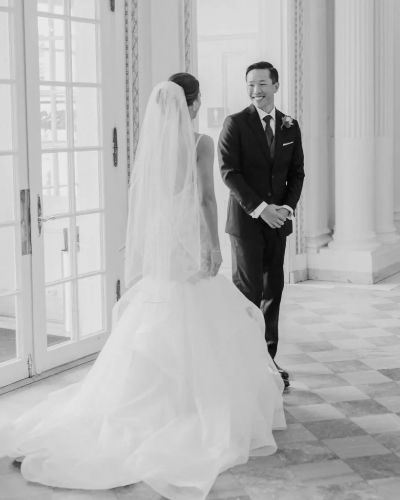 Groom smiles at the bride during a rainy-day first look inside the marble foyer at Tupper Manor