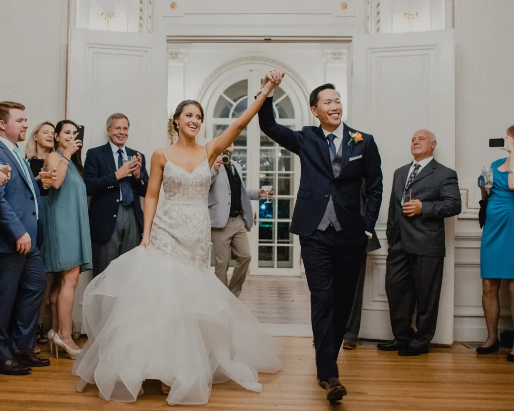 Newlyweds raise their hands entering the Tupper Manor ballroom as guests cheer and applaud